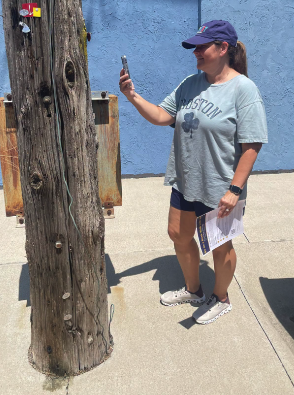 A patron on a sidewalk scanning a Book Walk QR code on a utility pole with her phone